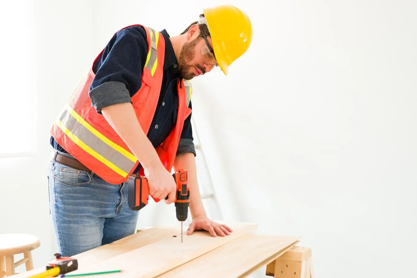 A professional engineer and contractor is drilling a wooden panel. A male carpenter wearing a safety helmet is working on building some furniture.